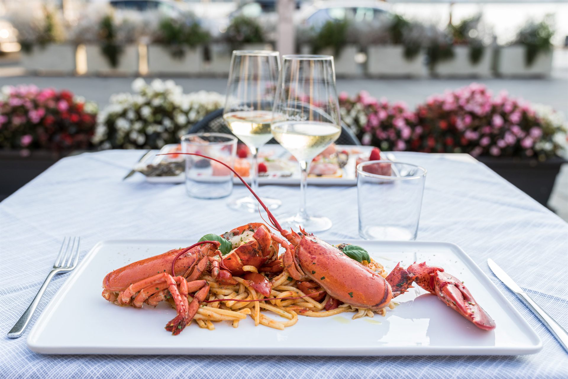 Tavolo apparecchiato in terrazza con spaghetti all'astice e due calici di vino bianco